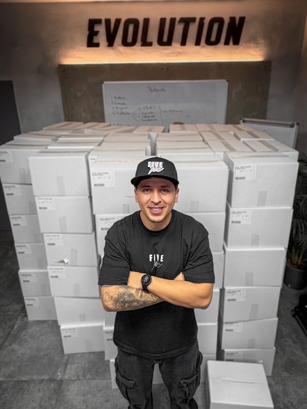 Joe Cuts con camiseta y gorra de FIVE AM, delante de los pedidos preparados